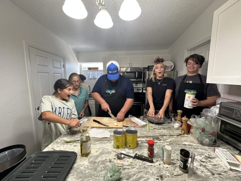 Students and a teacher prepare food together around a kitchen island